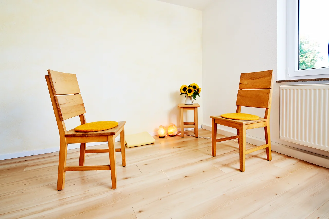 Der Praxisraum in Stuttgart-Degerloch: zwei einander zugewandte Holzstühle mit gelben Sitzkissen, Sonnenblumen und Salzlampen